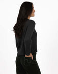 Model in studio wearing Rexie Jumper in Charcoal with Va Va Velour Pant in Khaki, close-up side view with hand in back pocket  