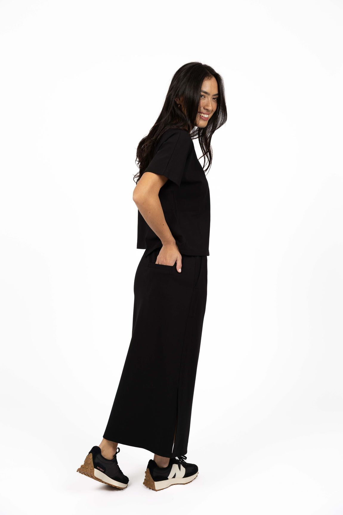 Model in studio wearing Roca Skirt in Black with matching Mosh Top and black sneakers, full-length back view  