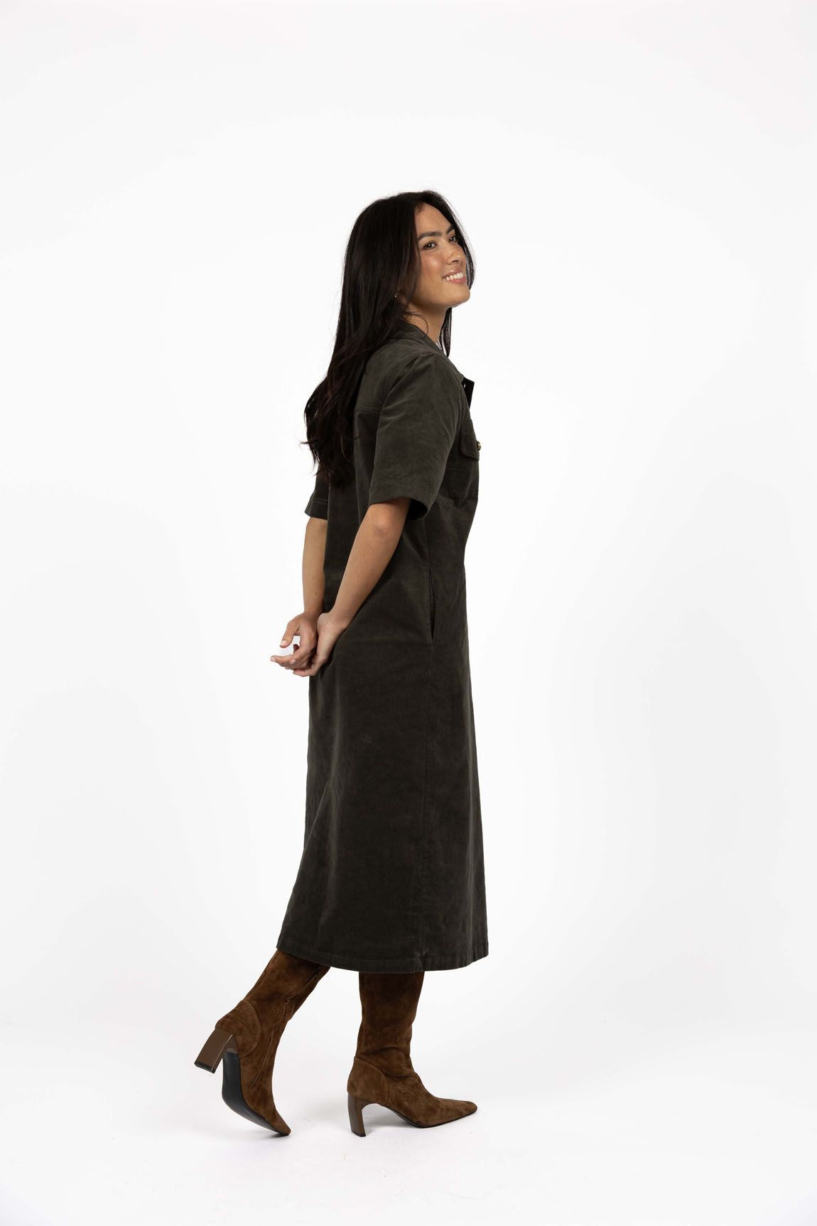 Model in studio wearing Amici Cord Dress in Khaki with brown boots, full-length side view  