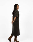 Model in studio wearing Amici Cord Dress in Khaki with brown boots, full-length side view  
