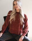 Model in lifestyle setting wearing Chenille Jumper in Rust with Va Va Velour Pant in Pine, close-up front view sitting on chair  