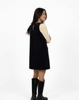 Model in studio wearing Nova Cord Dress in Indigo over the Mae Jumper in Buttermilk with black boots, full-length back view 